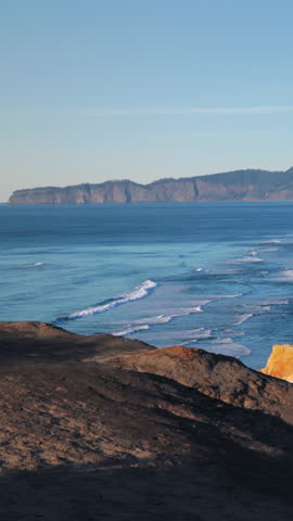 Wide vertical coastal view of Oregon Coast with rocky cliffs, rolling Pacific Ocean waves, textured shoreline, natural light, layered landscape and open horizon.