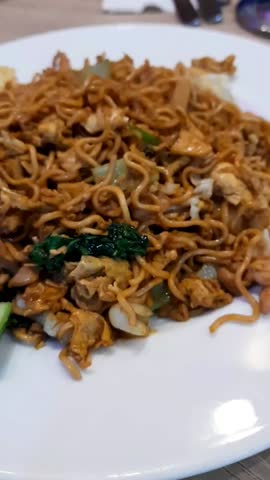 Mie goreng, traditional Indonesian fried noodles cooked with sweet soy sauce, vegetables, egg, and protein, served on a plate with cucumber pickles on the side. Fast food. vertical
