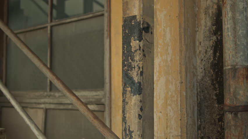 A smooth parallax move past a rusty metal staircase railing revealing a large dusty window with a wooden frame inside an old abandoned facility.