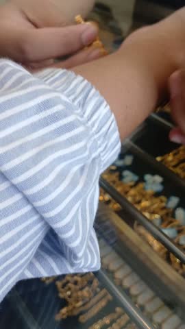 A person is trying on a 23 carat gold bracelet on a customer