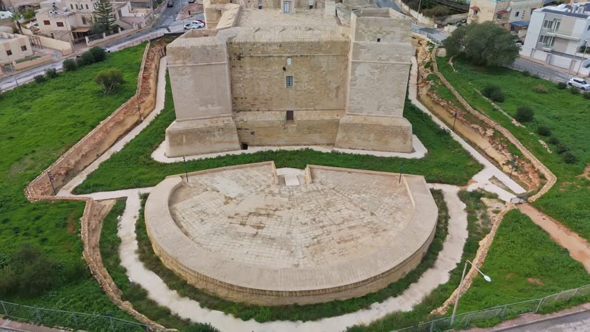 Ascending aerial reveal of Saint Thomas Tower, a medieval limestone watchtower in Marsaskala, Malta, surrounded by urban landscapes, showcasing its historical significance and Mediterranean charm.