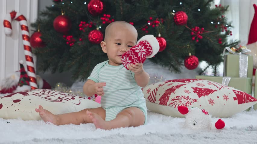 Joyful Cute Small Baby Boy Human Person Toddler Son Infant Child Sitting Near Beautiful Decorated Christmas Tree Holding Red Knitted Sock Looking Happy Feeling Curious With Holiday Ornaments In