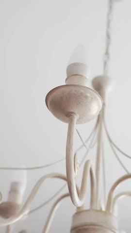 Vertical close-up of a dusty vintage chandelier on a white ceiling, showing worn interior lighting hardware and grime. Ideal for home maintenance, cleaning, renovation, or real estate b-roll.