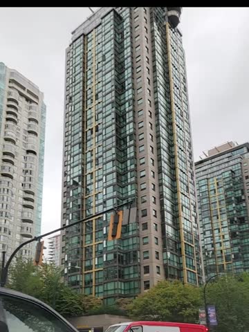 A slow-motion, low-angle shot of modern glass skyscrapers in downtown Vancouver, British Columbia, against an overcast sky.