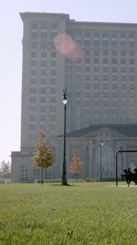 Vertical footage of people sitting on swing chairs outside Michigan Central Station in Detroit, Michigan. Urban landmark scene captured outdoors in daylight, ideal for city life, public spaces, travel