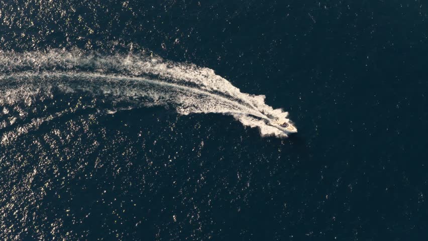 High angle drone shot tracking a boat driving on open sea, sunny evening in Italy
