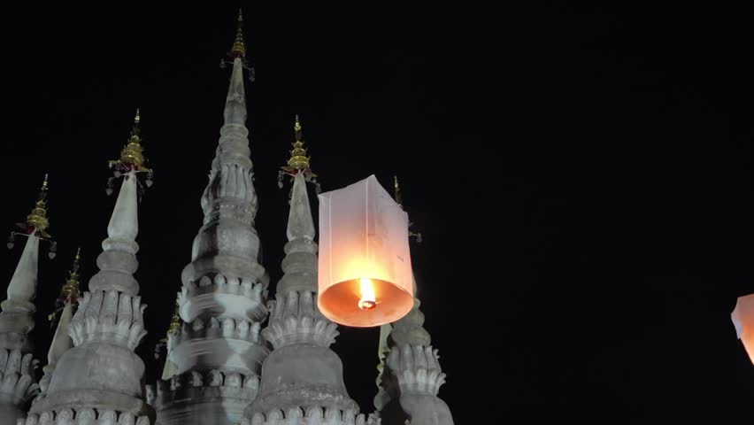 Paper lantern drifting through the night sky near a traditional Thai temple during festival celebrations.