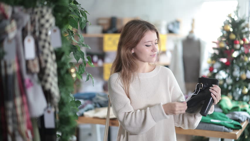 Young woman chooses stylish heeled ankle boots. Buyer holds ankle boots in hands and examines them before buying. Christmas shoes sale. High quality 4k footage
