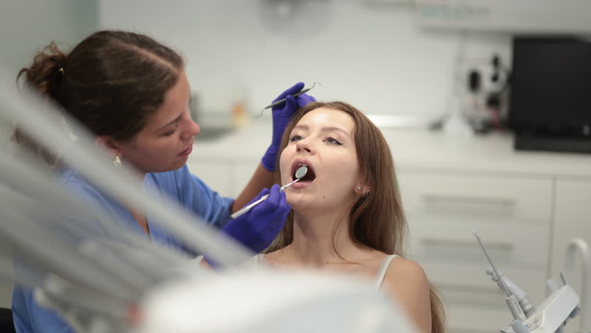 Young woman came for an examination and professional dental hygiene at a dental clinic. Woman dentist carefully examines the teeth of a client. High quality 4k footage