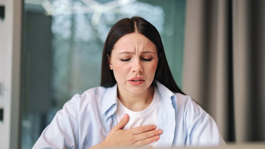 Woman experiences difficulty breathing, placing hand on chest. Expresses pain, shortness of breath, anxiety, and discomfort. Shows feelings of illness, urgent need for relief.