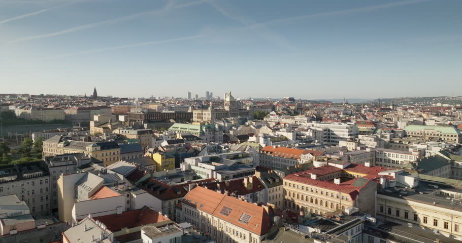 Prague aerial skyline over Old Town rooftops and modern districts under clear blue sky.