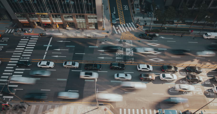 A vibrant urban street captures the continuous flow of vehicles moving through intersections, emphasizing the rhythm of city traffic. Time-lapse, Seoul, South Korea