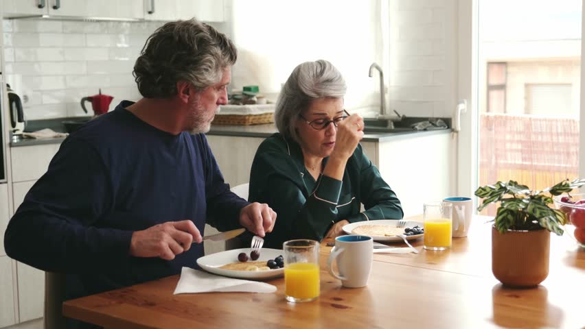 Senior couple in pajamas eating pancakes with berries and drinking orange juice in the morning