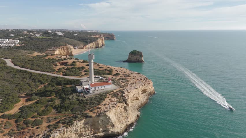 Aerial view flying past the lighthouse near Ferragudo, following the rugged coastal cliffs of the Algarve in Portugal.
