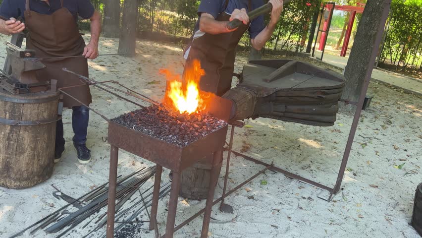 Blacksmith uses bellows to heat metal in forge, traditional craft