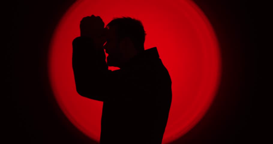 Dramatic silhouette of a man raising clenched fists in anger against a powerful red circular backlight, creating an intense emotional atmosphere. Ideal for concepts like rage, conflict, stress, emotio