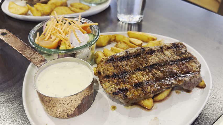 Juicy steak medium rare beef with baked potatoes on white plate served in restaurant. Top view, flat lay. Close up medium rare steak being cut on a plate with roast potatoes and creamy sauce. Served