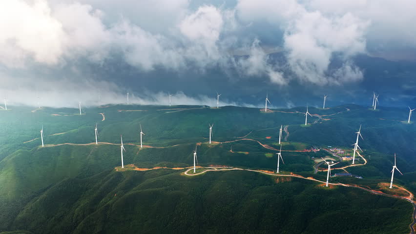 Aerial shot of many wind turbines on green mountain ridges under the thick clouds