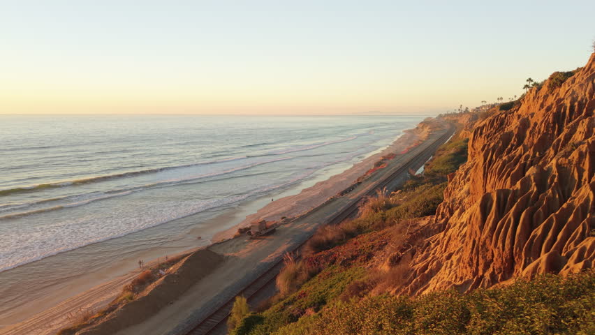 Sunset illuminates the sandstone cliffs at Torrey Pines in Del Mar, California. People walk on the beach.