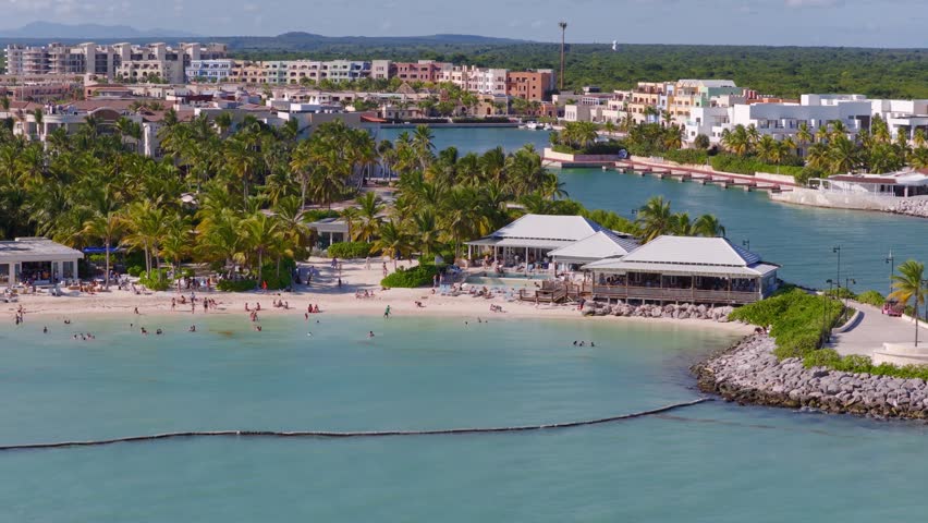 Clear-water bay in Punta Cana, Dominican Republic, with beachfront hotels and apartments, palm-lined shores and turquoise waters. Vibrant tropical island resort scene. Aerial panorama view.