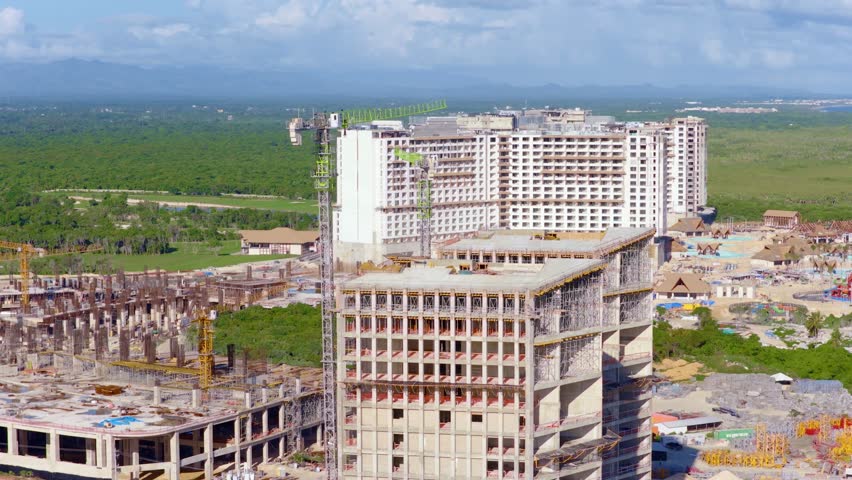 Aerial view of large hotel and resort development in Punta Cana, Dominican Republic, with tower cranes and rising structures against lush tropical landscapes. Rapid tourism growth on Caribbean island