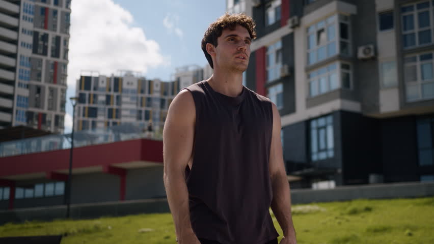 Cheerful motivated Caucasian sport man standing in confident pose strong position looking around stand in city carefree male guy smile proud sportsman relaxing after running jogging workout exercise