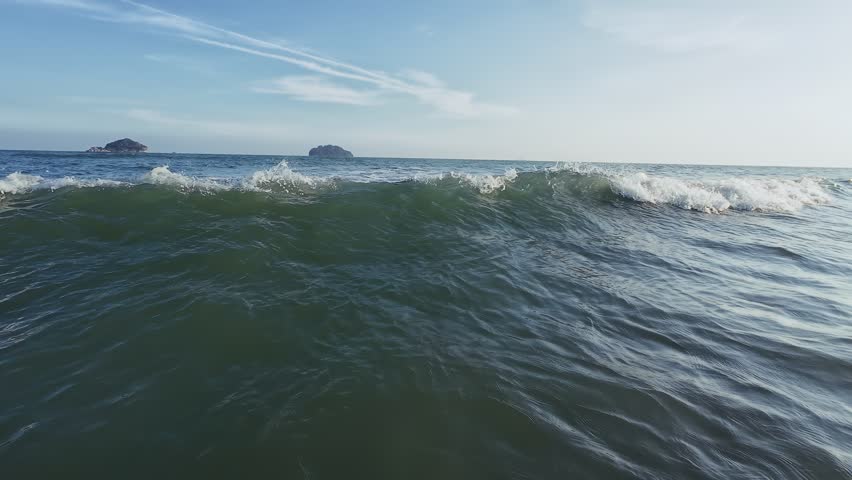 POV of bather in evening ocean as waves roll in golden droplets spray close water texture and shimmering surface under sun with distant shore backdrop visible