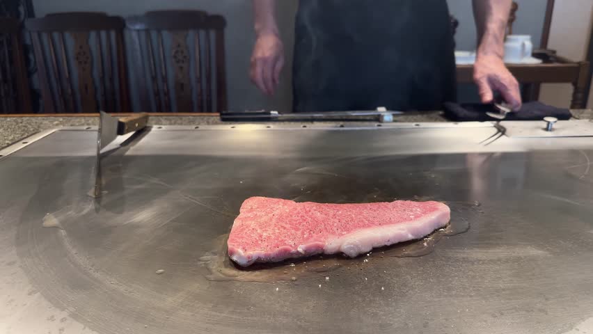 Professional chef cooking a premium wagyu Kobe beef steak on a hot teppanyaki grill plate