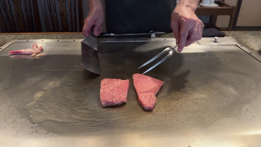 Japanese chef grilling marbled Kobe beef steak on a hot teppan plate in a restaurant