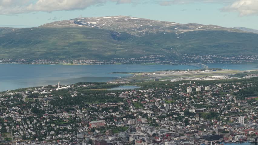 A Plane Descends Toward the Runway Beside the Fjord, With the City and Surrounding Mountains Spread Below, in Tromsø, Norway - Aerial Drone Shot