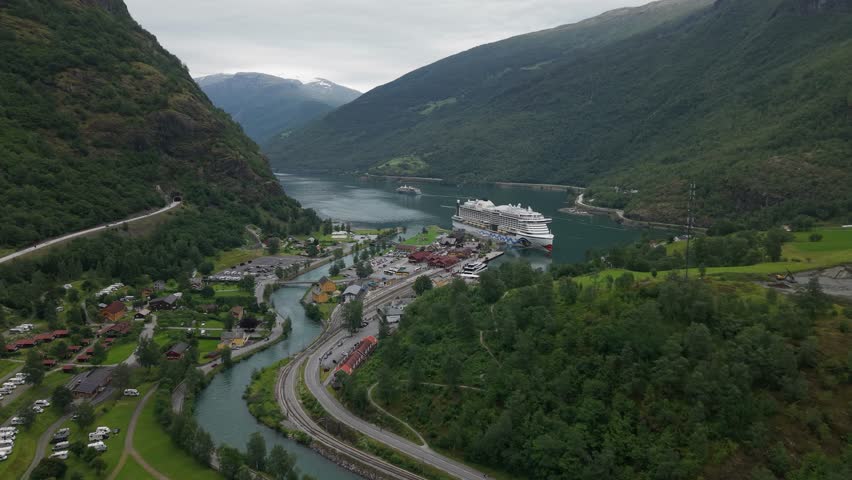 Flåm, Norway - A Large Cruise Ship is Docked by the Fjord Amid Houses, Railway Tracks, and a Winding River - Aerial Drone Shot
