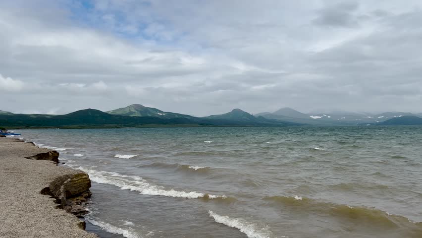 A high-altitude lake with clear water, surrounded by blue mountains and volcanoes on the horizon. A landscape captured at the edge of the earth, with untouched nature. The sound of the  waves and a gentle breeze in clear weather with beautiful clouds somewhere in New Zealand or Iceland. The waves slowly crash against the shore, creating a sense of tranquility and relaxation
Earth Day concept. 4k video