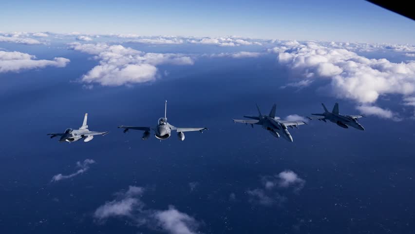 Aerial view of four military fighter jets flying in formation over the ocean and clouds during a naval exercise