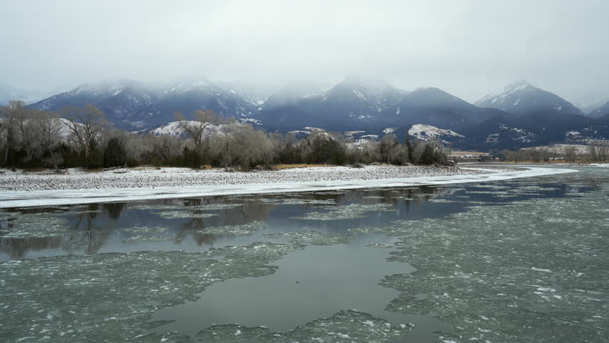 Snowy Mountains and bare trees beside Icy River