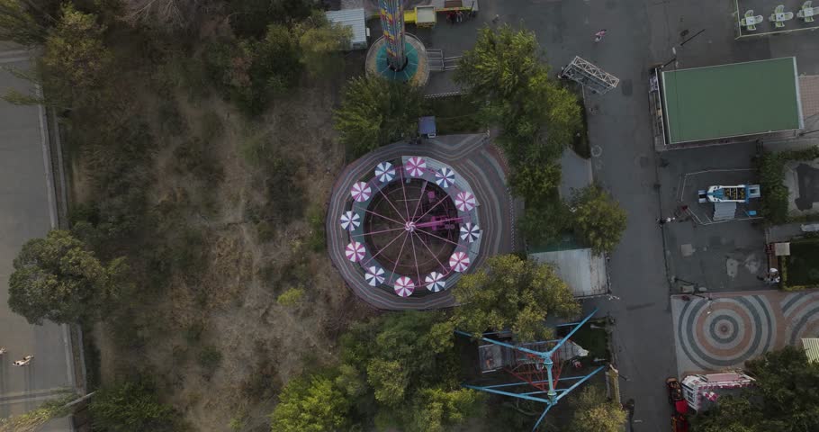 Aerial view of circular amusement park rides surrounded by trees and buildings, creating a vibrant, contrasting scene, Yerevan, Yerevan, Armenia.
