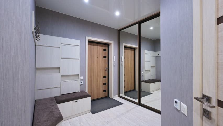 A modern hallway with light gray walls, wooden door, built-in storage, mirrored wardrobe, and a bench with storage — sleek and functional design.
