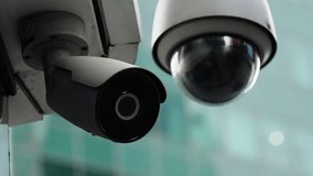 Close-up of outdoor security surveillance cameras, featuring a dome PTZ and a bullet unit mounted on a building bracket, monitoring an urban glass facade with reflections - Powered by Shutterstock - Get 15% off with code: PIKWIZARD15