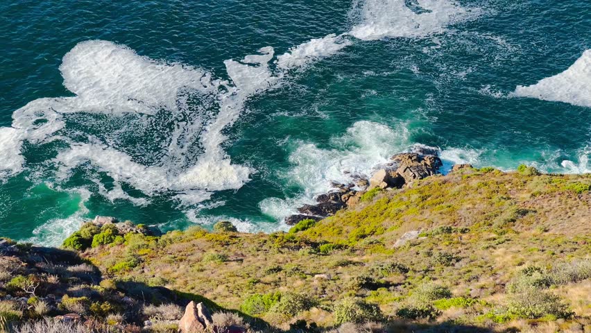 Aerial views of the Cape Peninsula in South Africa featuring dramatic Atlantic coastline, Chapman’s Peak Drive, Noordhoek Beach, Cape Point and the Cape of Good Hope. The footage showcases rugged cliffs, white sand beaches, turquoise ocean water and rolling mountains within Table Mountain National Park.

Filmed in bright summer daylight, the video captures scenic coastal roads, panoramic viewpoints, coastal fynbos vegetation and powerful waves meeting rocky shorelines. This iconic region at the southwestern edge of the African continent is known for its biodiversity, unspoiled landscapes and spectacular seascapes, making it ideal for travel, tourism, nature and adventure productions.