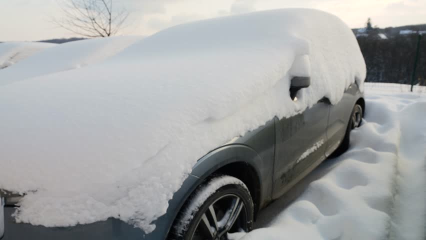 Deep snow covers cars in a winter parking lot. A heavy blizzard left a thick layer of white snow everywhere.