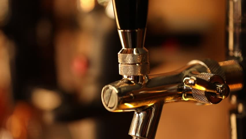 A bartender pours a foamy craft beer from a tap, filling a glass mounted on a wooden barrel. Dynamic shot highlighting fresh beverage service in a pub setting.
