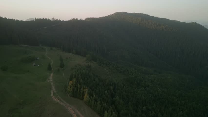 Flying over green forest at cloudy day with the mountains on horizon with glowing clouds. Carpathian mountains, Europe. 4k color corrected footage. Aerial view of classical european forest