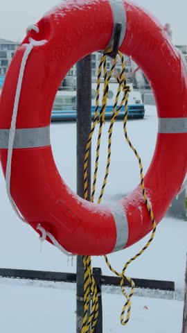 Vertical shot of orange Lifebuoy covered with icicles during winter under freezing conditions.