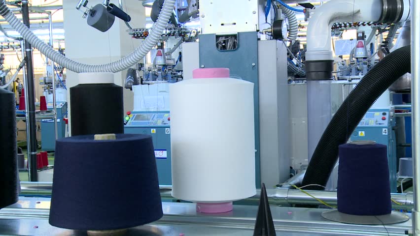 Large white, black, and blue yarn spools on industrial textile machinery in a modern factory setting. Manufacturing process of thread and fabric production.