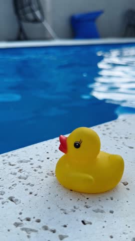 Close-up of a yellow rubber duck against a blue swimming pool water background. Shallow depth of field. Concept of hygiene, childhood, summer vacation, rubber duck debugging. 4k 60fps, High frame rate 
