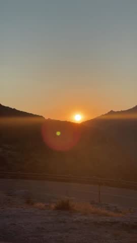 Sunrise Over Mountains and Road in Warm Light.

Early morning mountain landscape with road and hills illuminated by intense orange sunrise colors.
