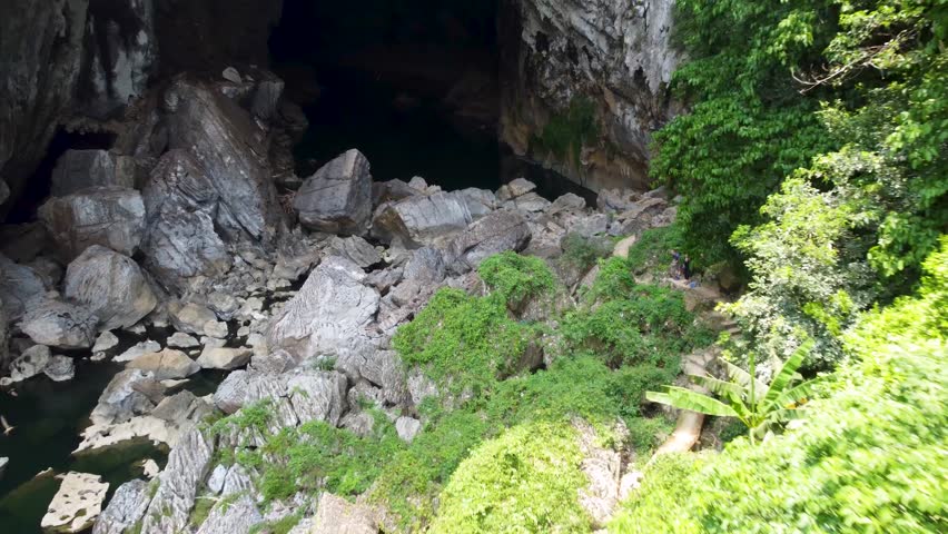 Bats fly above a river emerging from Xe Bang Fai Cave near Thakhek in central Laos surrounded by dense jungle and limestone cliffs.