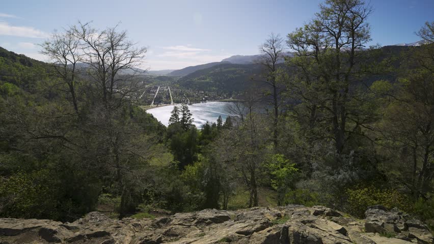 Elevated wide shot through autumn trees showing the city coastline and blue waters of Lake Lacar in the Patagonian Andes