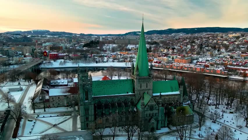 Aerial view of the historic Nidaros Cathedral and the city of Trondheim blanketed in snow under a warm sunset sky