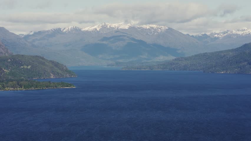 Elevated panoramic view of the deep blue Lake Lacar surrounded by forested hills and distant snow-capped peaks in Patagonia