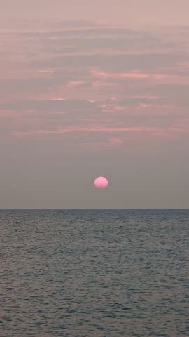 Sunrise sun shining over sea waters with rippled waves moving in slow motion captured in vertical format